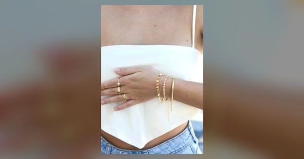 Detalhe das mãos com anéis e pulseiras Plaka sobre uma blusa branca.